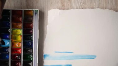 Sanatçı bir kağıt üzerine suluboya boya ile boyar. Çerçeve içinde bir fırça ile el.