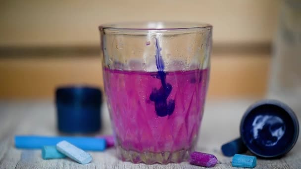 Toegevoegd een kwast druppel paarse inkt in een glas helder water. Water is gekleurd. De creativiteit van de kunstenaar. Een druppel van blauwe verf is toegevoegd — Stockvideo