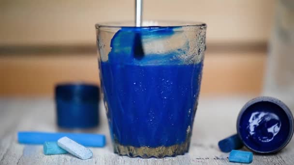 Dans un verre transparent d'eau ajouté avec une goutte de pinceau de peinture bleue et remuer.L'eau est tachée . — Video