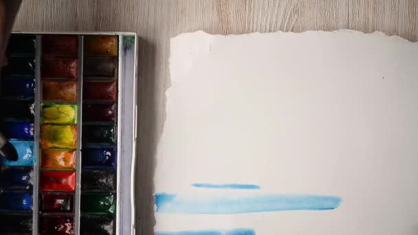 der Künstler malt mit Aquarellfarben auf ein Blatt Papier. Hände mit einem Pinsel im Rahmen.