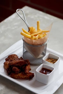 Parşömen kağıt üzerine tavuk kanadı sosu ketçap ve patates kızartması bir metal stand