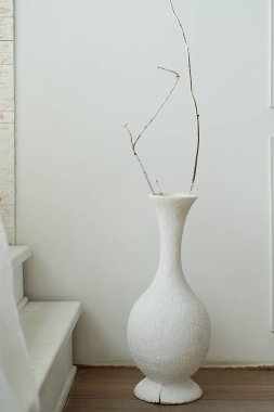 Kuru dal ile beyaz aranjman beyaz bir duvar önünde duruyor. Oda minimalist tasarımı