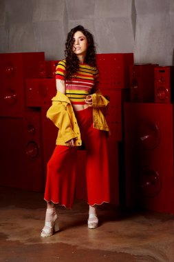 Studio moda çekim. Kız parlak bir kıyafet, üst ve altına kırmızı ve turuncu renklerde alevlendi. Esmer kıvırcık saçlı