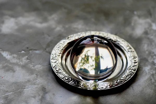 The glass ball lies on an old saucer. Grey concrete background — Stock Photo, Image