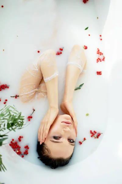 Lichte Studio.Delicate en sensuele sfeer van vrede en rust. Relaxation.Portrait van een mooi meisje met dikke lippen, sierlijke dunne polsen, nat haar. Liggend in een bad van melk met Rowan. — Stockfoto