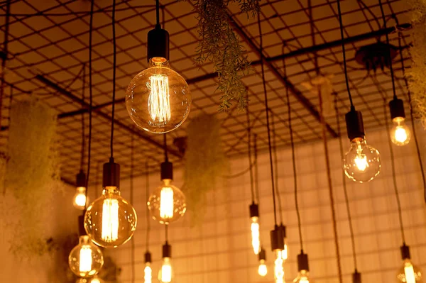 Ancient Edison lamps on black wires.Warm light in the design of the cafe. — Stock Photo, Image