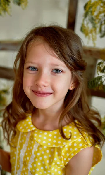 Retrato de una niña sonriente con un vestido amarillo de 6 años. Oreja perforada.Ojos azules, pelo largo . —  Fotos de Stock