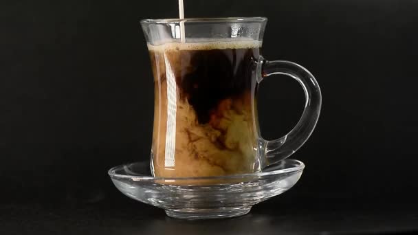 Un chorrito de leche se vierte en el café caliente al vapor. Vidrio transparente, café negro en turco. Bebida caliente sobre un fondo oscuro . — Vídeos de Stock