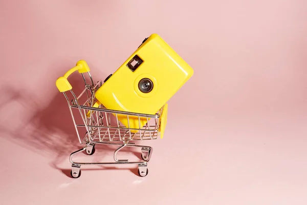 Venta y compra de equipos de fotografía.Cámara amarilla en una canasta sobre un fondo rosa. Creativo, un lugar para el texto . — Foto de Stock