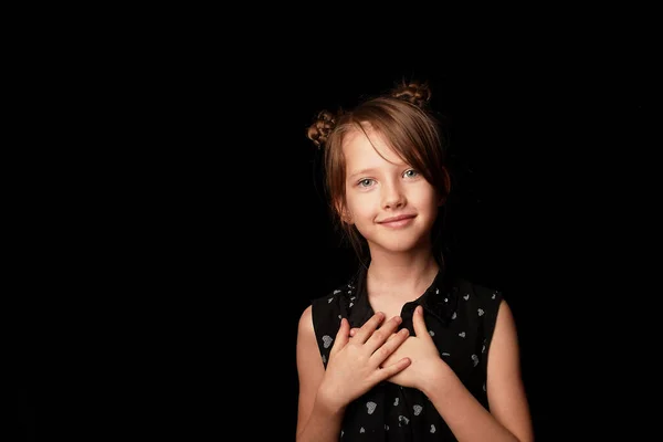 Una niña de 6 años sobre un fondo negro. Las manos están unidas al pecho, un signo de aceptación y gratitud . — Foto de Stock