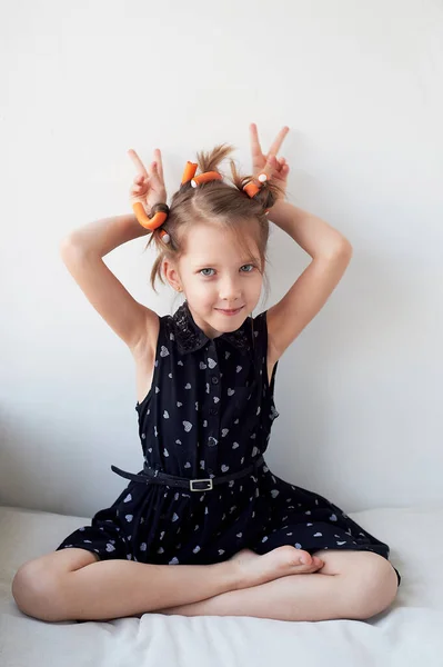 Una niña de 6 años con rulos en la cabeza, tonteando. La búsqueda de la belleza.Niños alegrías. Aislado sobre un fondo blanco . —  Fotos de Stock