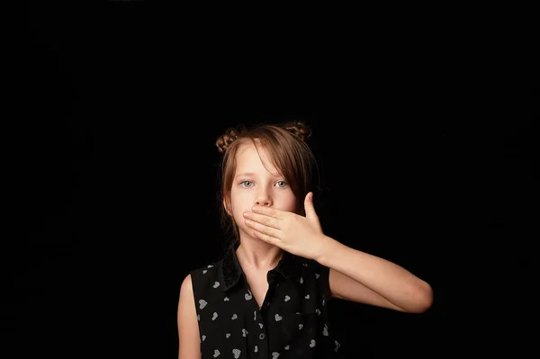 Egy 6 éves lány, sötét háttérrel. A tenyerével takarta el a száját. Nem a gonoszról beszélek. Csend és csend jeléül.. — Stock Fotó