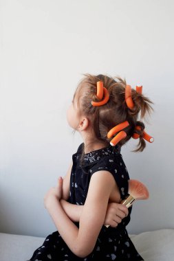 A 6-year-old girl with curlers on her head, fooling around. The pursuit of beauty.Childrens joys. Isolated on a white background. clipart