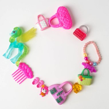 Pembe tonda küçük bir kızın oyuncakları. Deniz tarakları, el çantaları, atlar, boncuklar. Çocuk zenginliği. Beyaz bir arka planda dizilmiş.