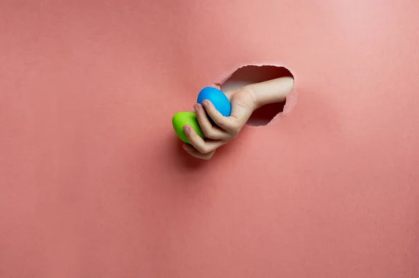 Mão em um buraco de papel rosa.Ovos pintados para a Páscoa. Tendência. Azul, verde sobre um fundo rosa . — Fotografia de Stock