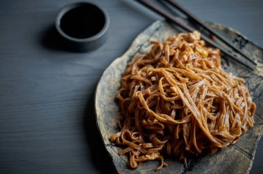 Teriaki soslu karabuğday eriştesi. Tahta sopalarla. Kil bir plaka ve gri bir arka planda.