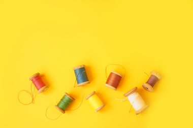 Sarı arka planda iplikleri olan renkli bobinler. El işleri ve dikiş. Üst görünüm