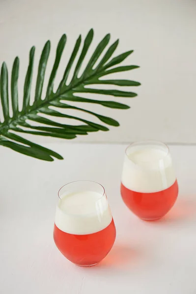 Cocktail em copos transparentes. Camadas de geleia e chantilly. Coquetel de morango em um fundo branco com uma folha de palmeira. . — Fotografia de Stock