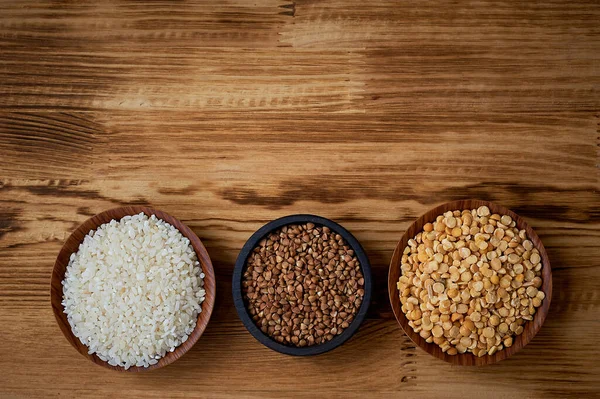 Useful food. The evils and the legumes.Buckwheat, rice, peas in flats on a wooden background. Simple and healthy food. — Stock Photo, Image