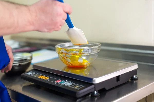 Man weighs caramel in a glass bowl on an electronic balance