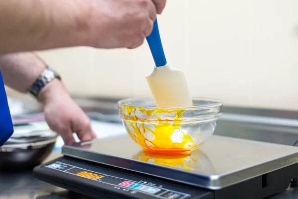 Man weighs caramel in a glass bowl on an electronic balance