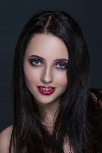 Mooie jonge brunette vrouw met perfecte huid close-up portret op donkere grijze achtergrond. Golvend kapsel, heldere luxe make-up, rode lippen. — Stockfoto