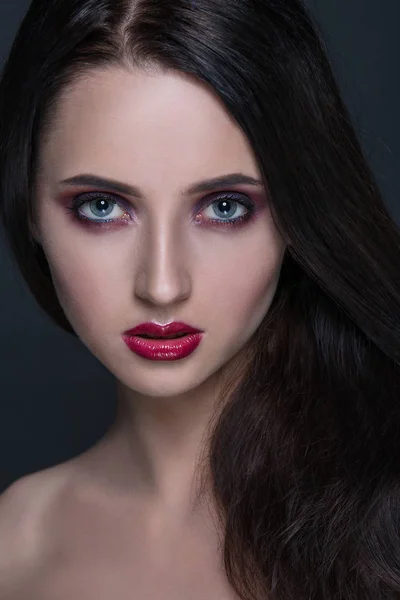 Mooie jonge brunette vrouw met perfecte huid close-up portret op donkere grijze achtergrond. Golvend kapsel, heldere luxe make-up, rode lippen. — Stockfoto