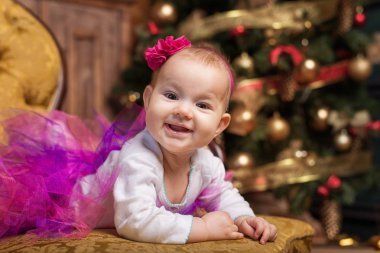 Noel ağacı önünde kanepede döşenmesi şirin bebek kız pembe etek ve kırmızı kafa bandı, giyiyor. Gülümseyen yürümeye başlayan çocuk.