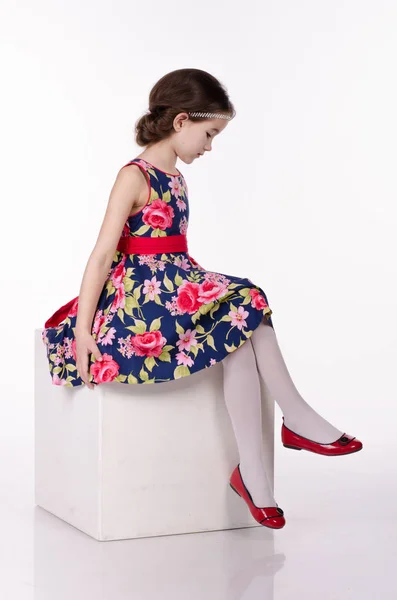Kislány ruha viselése virágok elszigetelt fehér background. Ő ül a kocka. Stúdió felvétel. — Stock Fotó