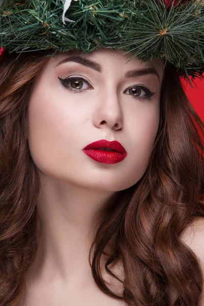 Kerstmis of Nieuwjaar schoonheid meisje portret geïsoleerd op rode achtergrond. Mooie vrouw met luxe make-up en kerst krans op hoofd. Kerstsfeer. — Stockfoto