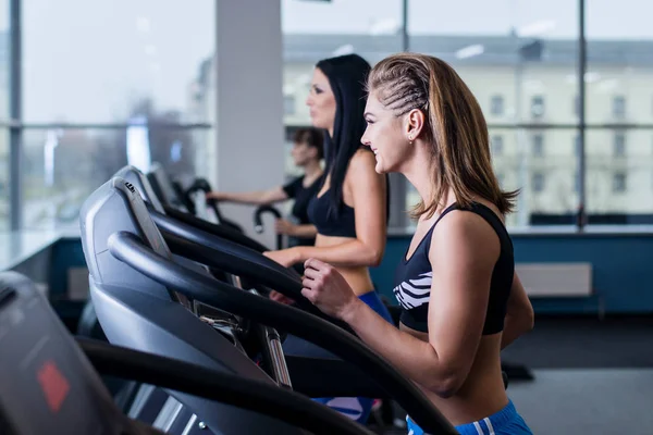 Sexy fit mulheres correndo em esteiras na academia moderna. Jovens meninas saudáveis fazendo exercício de corrida na esteira na academia . — Fotografia de Stock