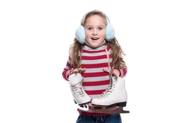 Lovely smiling little girl wearing colorful striped sweater and headdress, holding skates isolated on white background. Winter clothes. — Stock Photo, Image