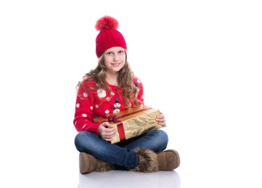 Küçük kız kırmızı örgü kazak ve Noel hediyesi holding şapkası giyen kıvırcık saç modeli ile gülümseyen sevimli beyaz arka plan üzerinde izole. Kış giysileri ve Noel kavramı.