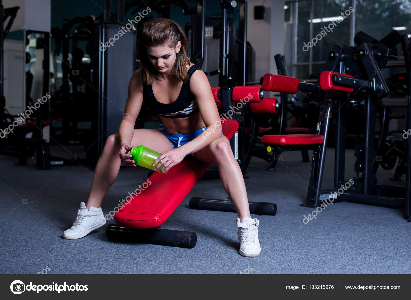 Sexy fitness woman in sportswear resting after dumbbells exercises in gym.  Beautiful girl with perfect fitness body drinking from shaker bottle after  gym training. Stock Photo by ©artyme 133215976