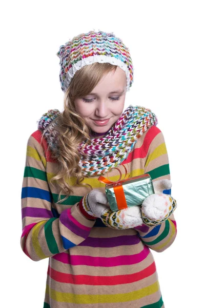 Sorrindo menina bonita vestindo cachecol de malha colorido, chapéu e mitenes, segurando presente de Natal isolado no fundo branco. Roupas de inverno e conceito de Natal . — Fotografia de Stock