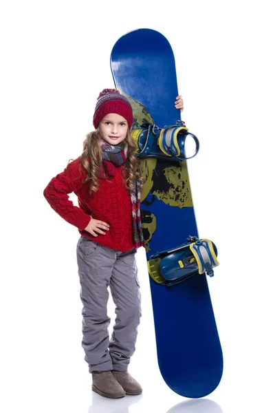 Lächelndes kleines Mädchen mit lockiger Frisur in Strickpullover, Schal, Mütze und Handschuhen mit blauem Snowboard, isoliert auf weiß. Daumen hoch. Winterbekleidung und Sportkonzept. — Stockfoto