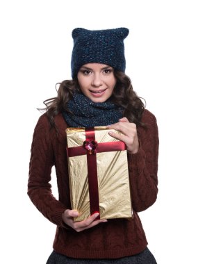 Noel hediyesi tutan örme kazak, atkı ve şapka, oldukça neşeli seksi genç kadın. Beyaz arka plan üzerinde izole. O gülümseyen ve duygular gösterilen. Kış giysileri.