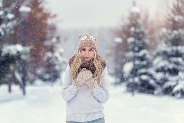 Atractiva joven rubia caminando en el bosque de invierno. Mujer bonita en invierno al aire libre. Llevando ropa de invierno. Jersey, bufanda, gorro y manoplas de punto . — Foto de Stock