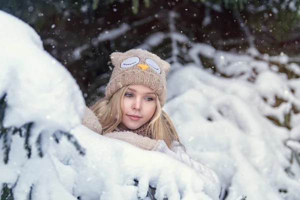 Atractiva joven rubia caminando en el bosque de invierno. Mujer bonita en invierno al aire libre. Llevando ropa de invierno. Jersey, bufanda, gorro y manoplas de punto . — Foto de Stock