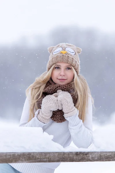Menina loira sorrindo atraente andando na floresta de inverno. Mulher bonita no inverno ao ar livre. Vestindo roupas de inverno. Camisola de malha, cachecol, chapéu e mitenes . — Fotografia de Stock