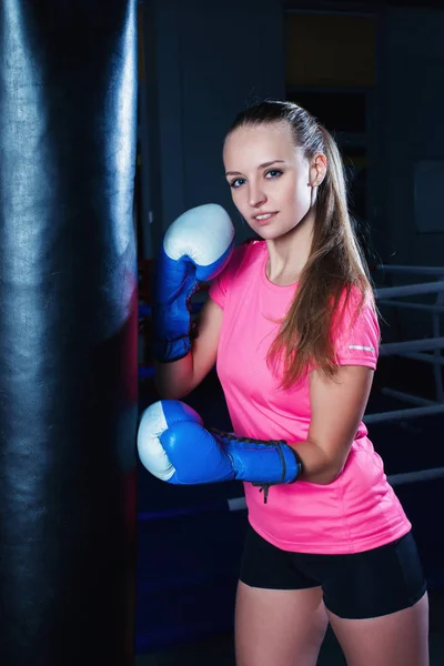 Ελκυστική νεαρή γυναίκα με μπλε γάντια του μποξ στο γυμναστήριο του αθλητισμού. Όμορφο θηλυκό μπόξερ με σάκο ζουμπάρισμα. — Φωτογραφία Αρχείου