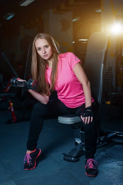 Menina desportiva atraente fazendo exercícios com halteres no ginásio. Mulher fitness bonita trabalhando em seu bíceps . — Fotografia de Stock