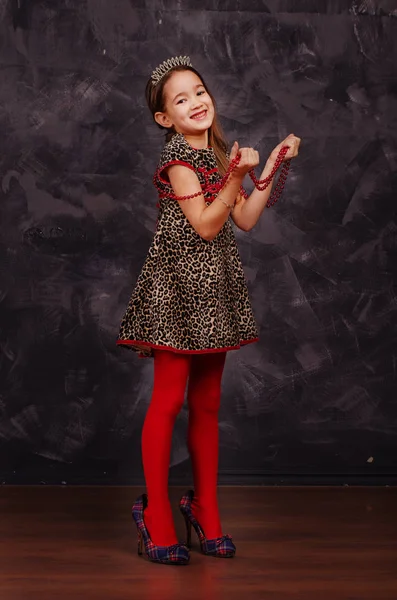 Szép mosolygó kislány gyönyörű ruha viselése. Ő visel piros gyöngyök, és tartja őket a kezét. Stúdió felvétel. — Stock Fotó