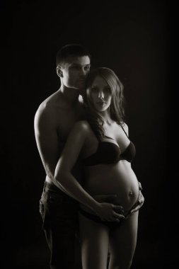 Monochrome portrait of happy loving couple in a moment of love and tenderness. Pregnant woman with hands over tummy. Black and white photo. clipart