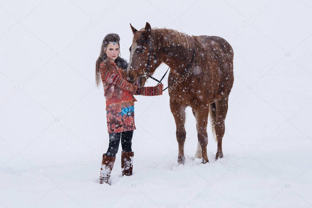 Native indian woman with traditional makeup and hairstyle in snowy winter. Beautiful girl in ethnic dress hugging a horse.