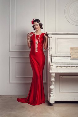 Added veya Added kadeh martini yakınındaki piyano ile kırmızı elbise tarzı genç güzel kız. Vintage tarzı güzel bir kadın. Eski moda makyaj ve retro parmak dalga saç modeli.