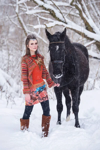 Mulher indígena nativa com maquiagem tradicional e penteado no inverno nevado. Menina bonita em vestido étnico na floresta com um cavalo . — Fotografia de Stock