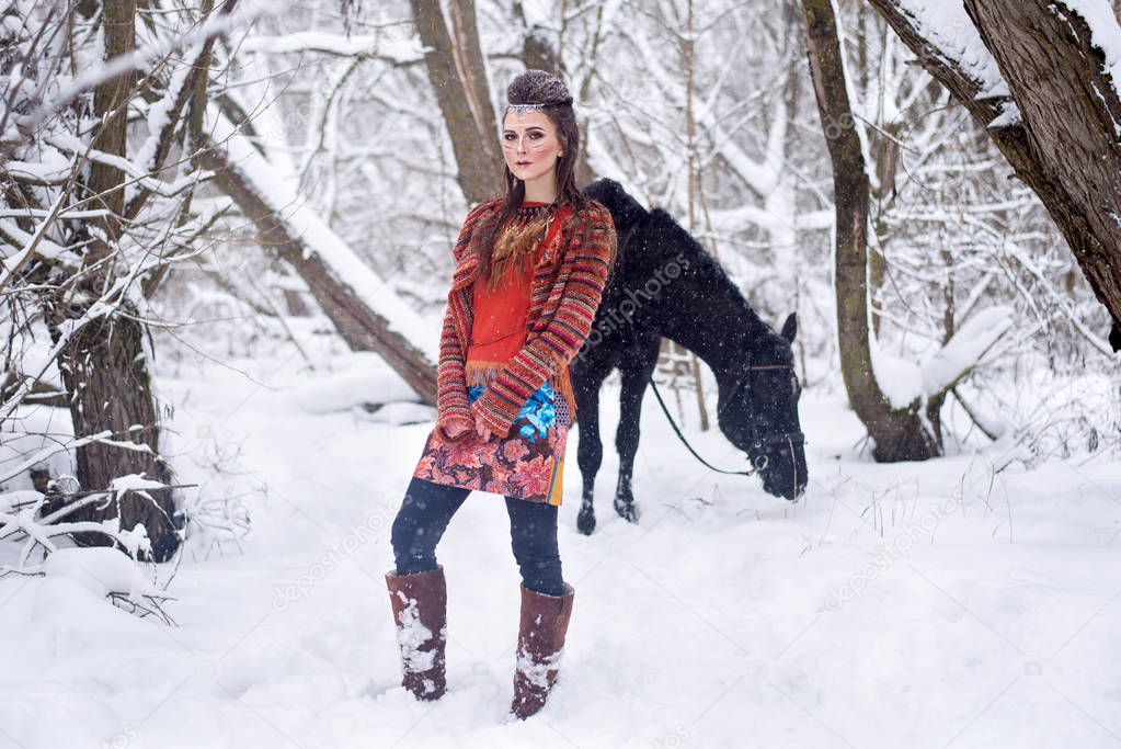 Native indian woman with traditional makeup and hairstyle in snowy winter. Beautiful girl in ethnic dress in the forest with a horse.