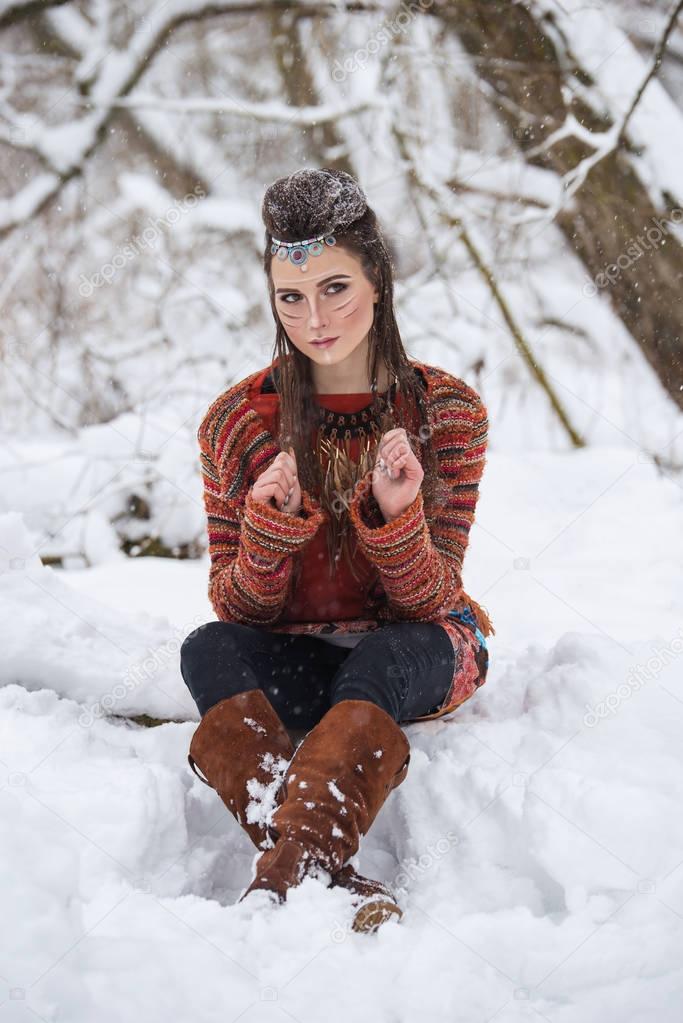 Portrait of native indian woman with traditional makeup and hairstyle in snowy winter. Beautiful girl in ethnic dress in the forest.