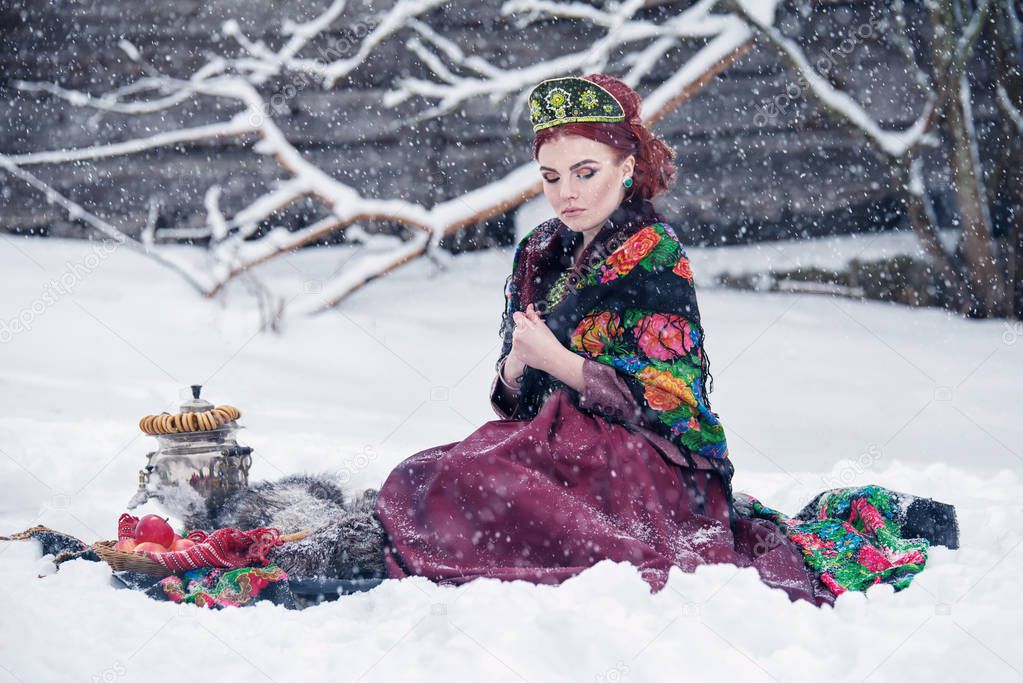 Portrait of a gorgeous young woman in russian style dress on a strong frost in a winter snowy day with apples and samovar. Russian model girl in traditional headdress.